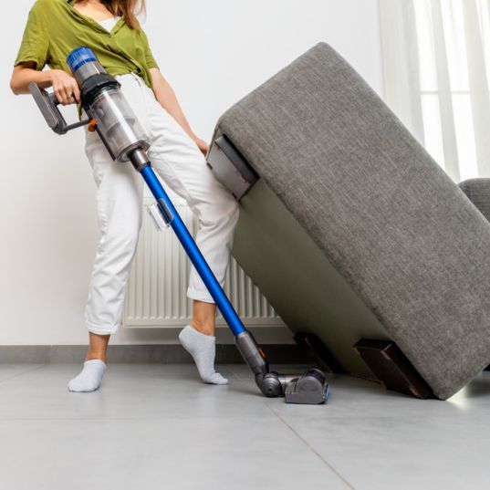 mujer levantando sofa y pasando aspiradora